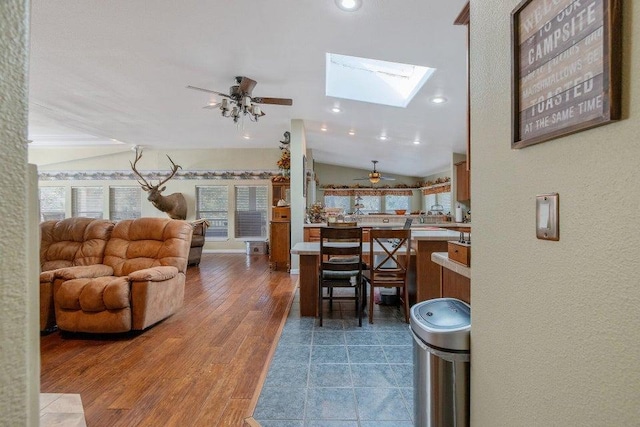 dining area with dark wood-type flooring, ceiling fan, and vaulted ceiling with skylight