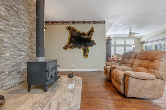 living room with ornamental molding, wood-type flooring, ceiling fan, and a wood stove