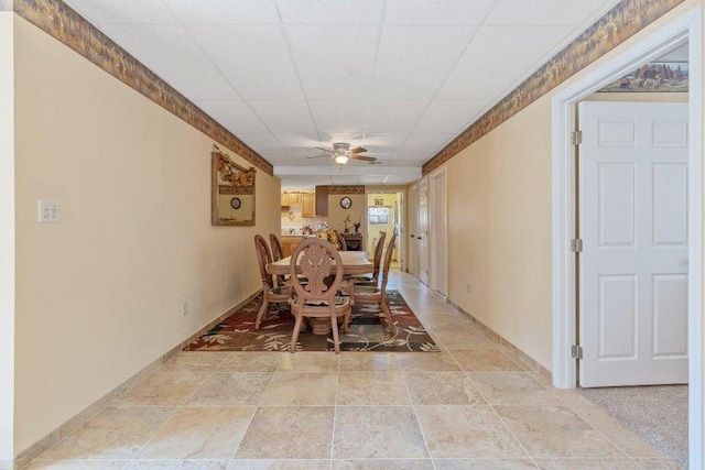 dining area featuring baseboards, a drop ceiling, stone finish flooring, and a ceiling fan