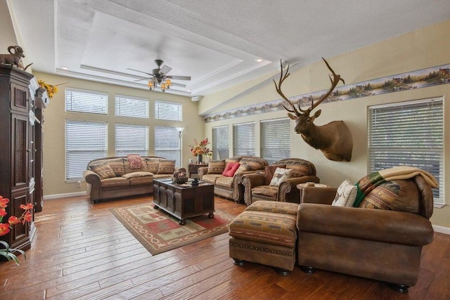 living room with wood-type flooring, baseboards, a textured ceiling, a raised ceiling, and a ceiling fan