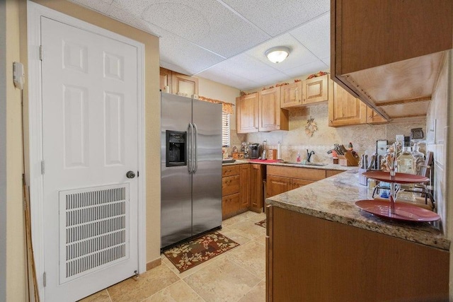 kitchen with light stone countertops, backsplash, stainless steel fridge with ice dispenser, sink, and light tile patterned flooring