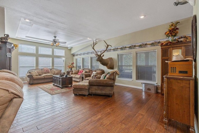 living area with baseboards, recessed lighting, a ceiling fan, a raised ceiling, and dark wood-type flooring