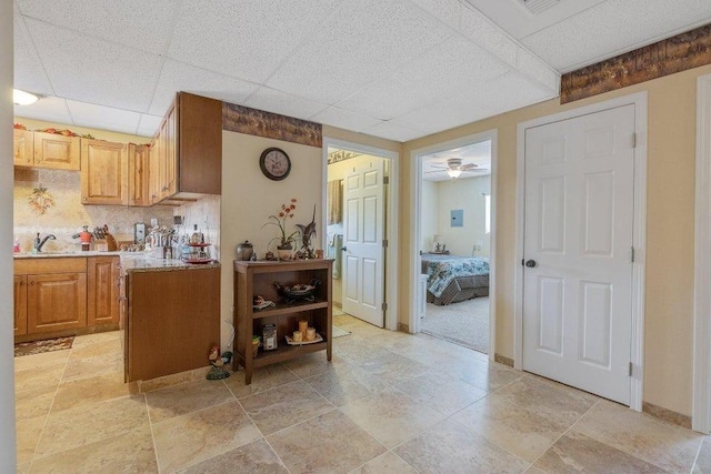 kitchen with light countertops, baseboards, decorative backsplash, a drop ceiling, and a sink