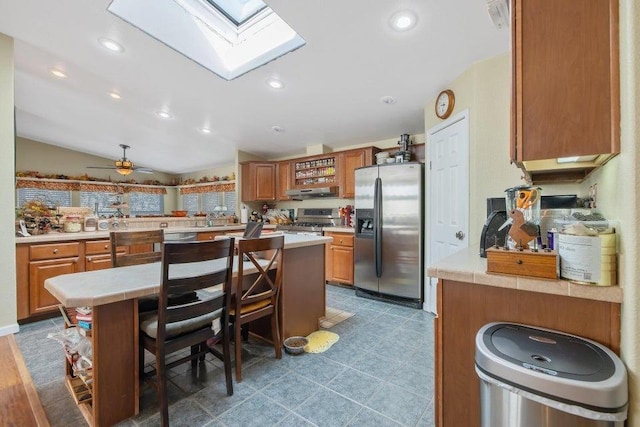 kitchen featuring brown cabinets, light countertops, lofted ceiling with skylight, and stainless steel appliances