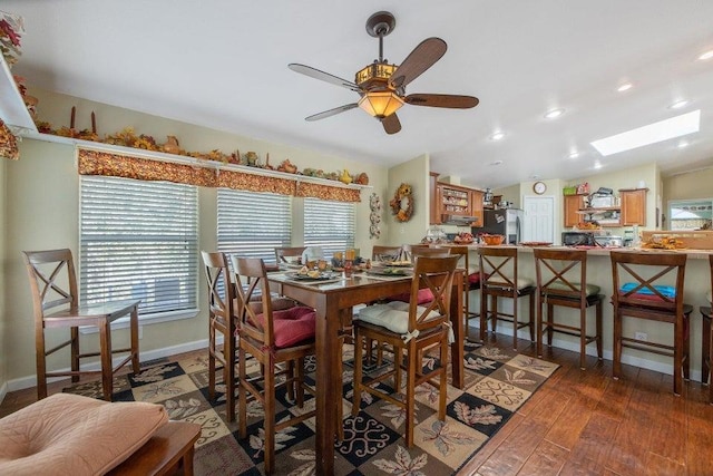 dining space featuring vaulted ceiling with skylight, hardwood / wood-style floors, and ceiling fan