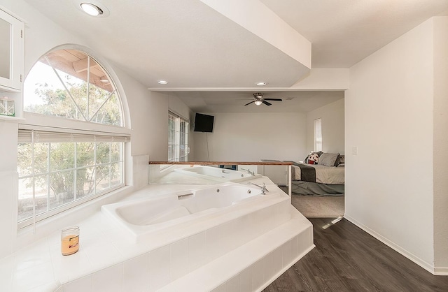 bathroom with wood-type flooring, ceiling fan, and tiled bath