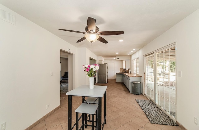 kitchen featuring a breakfast bar area, gray cabinetry, light tile patterned floors, ceiling fan, and stainless steel fridge