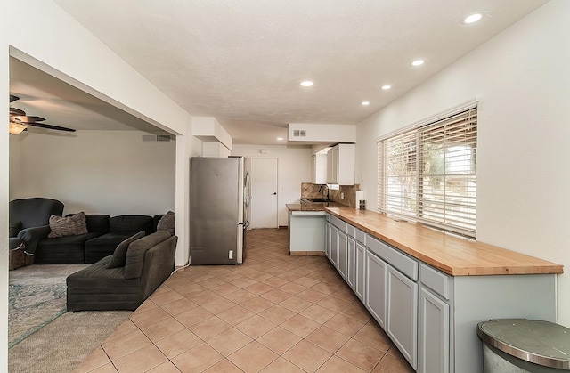 kitchen featuring stainless steel refrigerator, light tile patterned flooring, wood counters, and sink