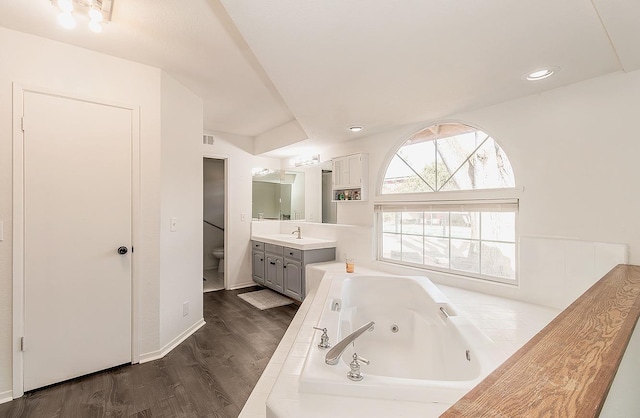 bathroom featuring toilet, hardwood / wood-style flooring, tiled tub, and vanity