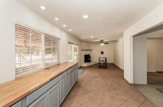 kitchen with light tile patterned floors, butcher block countertops, gray cabinetry, a fireplace, and ceiling fan