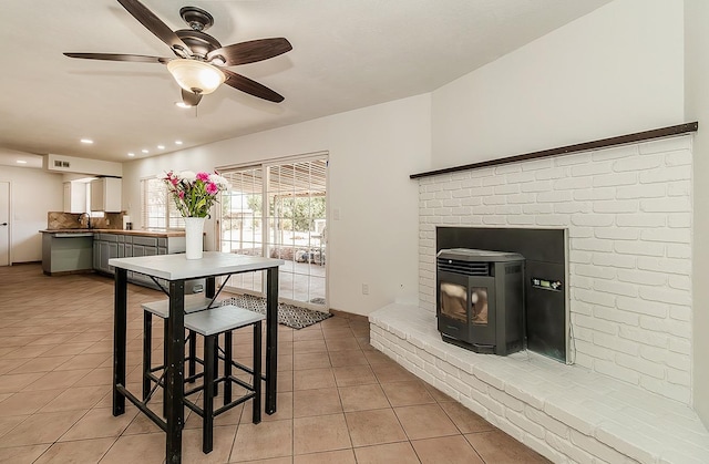 kitchen featuring kitchen peninsula, a wood stove, white cabinetry, light tile patterned flooring, and ceiling fan