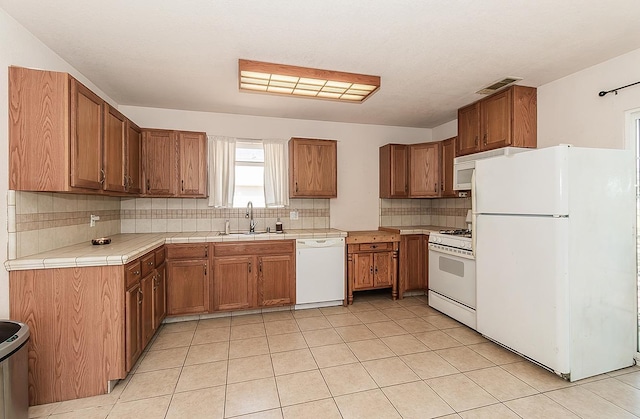 kitchen with white appliances, tile counters, light tile patterned floors, decorative backsplash, and sink