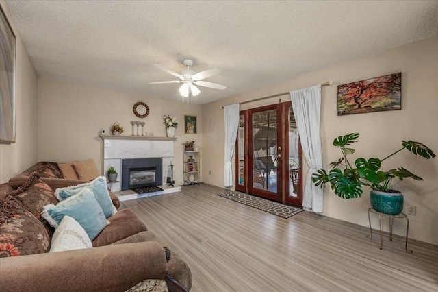 living room featuring a textured ceiling, ceiling fan, a tiled fireplace, and hardwood / wood-style flooring