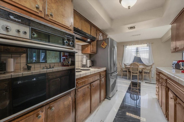 kitchen with backsplash, oven, a raised ceiling, white gas stovetop, and tile counters