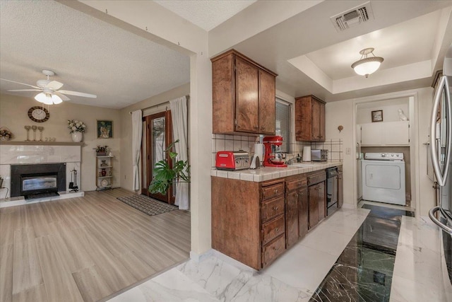 kitchen with tile countertops, tasteful backsplash, a premium fireplace, ceiling fan, and washer / clothes dryer