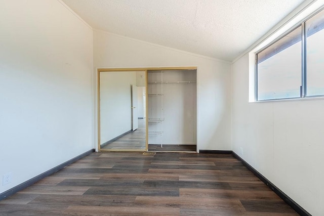 unfurnished bedroom featuring dark wood-style floors, crown molding, lofted ceiling, a closet, and a textured ceiling