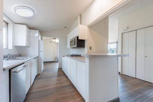 kitchen with dark wood-style floors, stainless steel appliances, light countertops, white cabinetry, and a sink