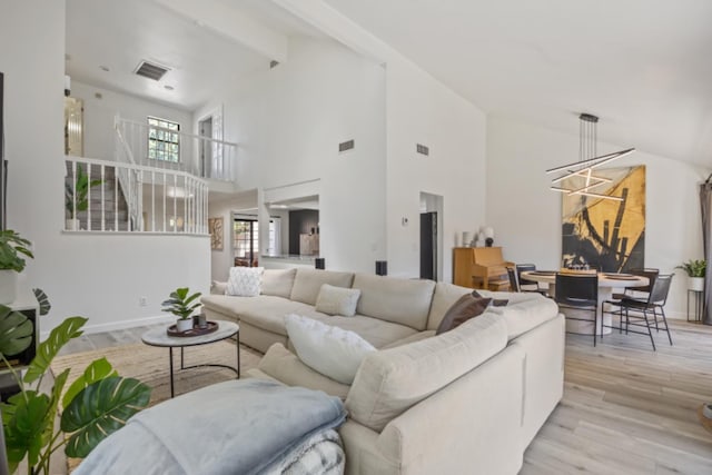 living room with beamed ceiling, a chandelier, high vaulted ceiling, and light wood-type flooring