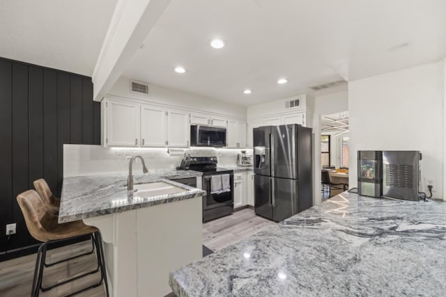 kitchen featuring kitchen peninsula, white cabinets, appliances with stainless steel finishes, light wood-type flooring, and sink