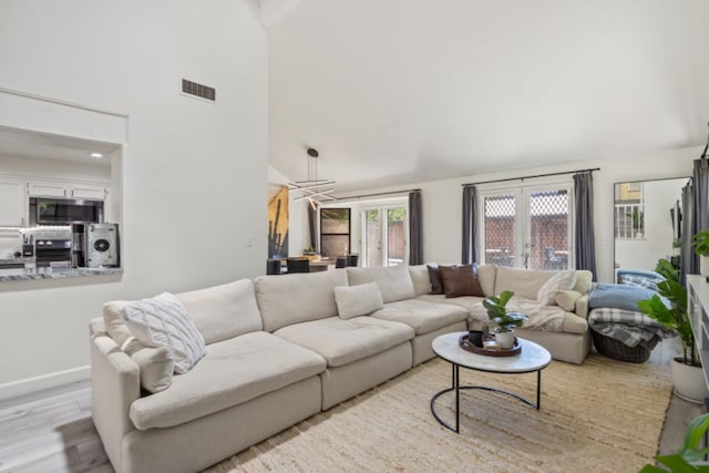 living room featuring french doors, light hardwood / wood-style flooring, and a towering ceiling