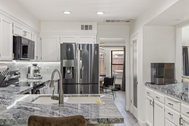 kitchen with appliances with stainless steel finishes, light hardwood / wood-style flooring, white cabinets, and light stone counters