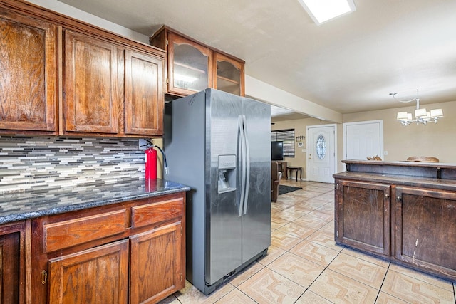 kitchen featuring an inviting chandelier, tasteful backsplash, stainless steel fridge with ice dispenser, dark stone countertops, and light tile patterned floors