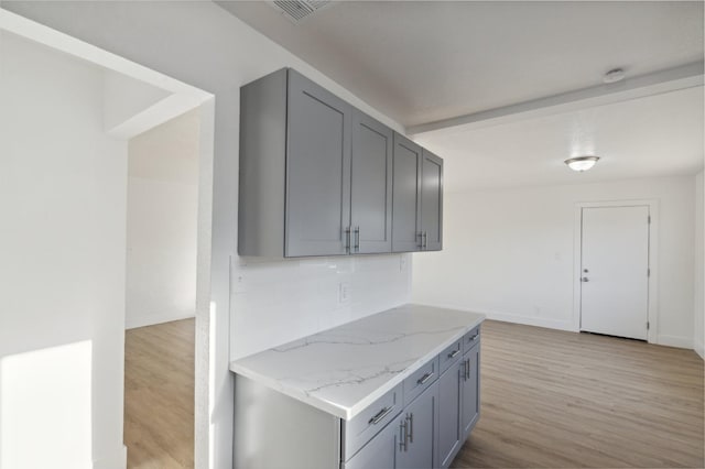 kitchen featuring light wood-type flooring, light stone counters, and gray cabinets