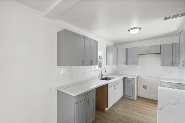 kitchen featuring gray cabinetry, light stone countertops, light hardwood / wood-style floors, sink, and tasteful backsplash