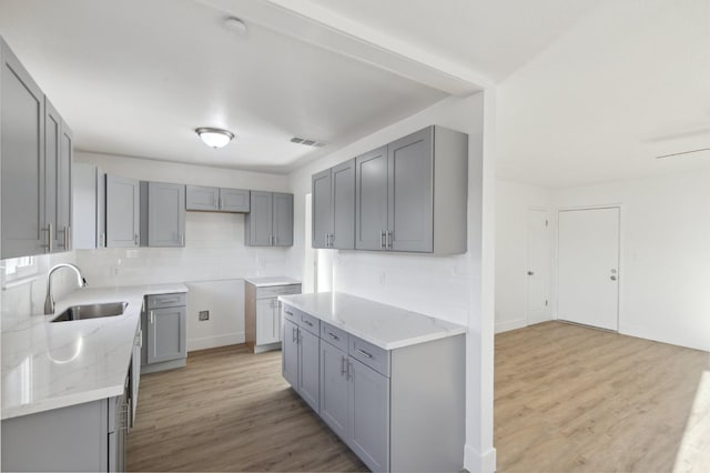 kitchen with gray cabinets, light wood-type flooring, decorative backsplash, and sink