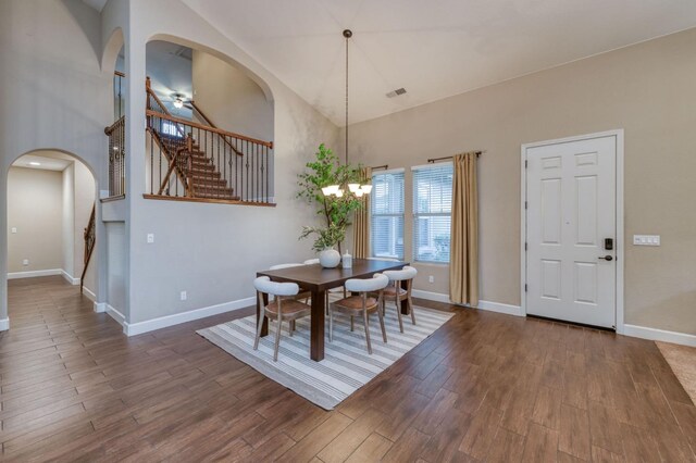 dining space with dark wood-type flooring, a high ceiling, and ceiling fan with notable chandelier