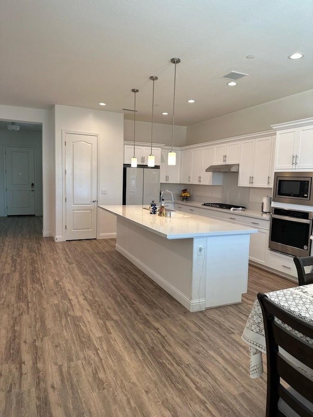 kitchen featuring a kitchen island with sink, pendant lighting, hardwood / wood-style floors, stainless steel appliances, and white cabinets