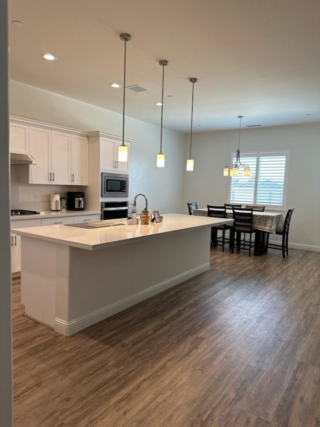 kitchen featuring dark hardwood / wood-style flooring, appliances with stainless steel finishes, an island with sink, hanging light fixtures, and white cabinets