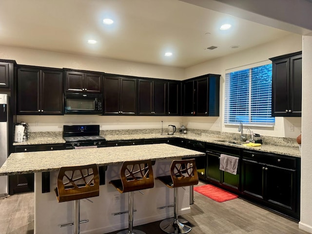 kitchen with black appliances, a breakfast bar area, a center island, and sink