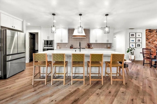 kitchen featuring appliances with stainless steel finishes, light hardwood / wood-style flooring, white cabinets, and hanging light fixtures