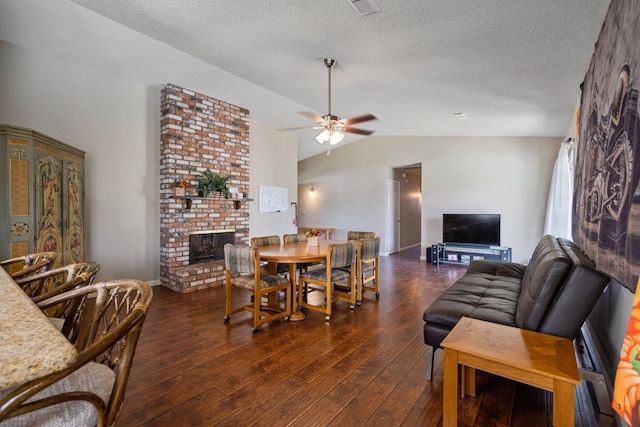 dining room featuring ceiling fan, a textured ceiling, dark wood-type flooring, a fireplace, and vaulted ceiling