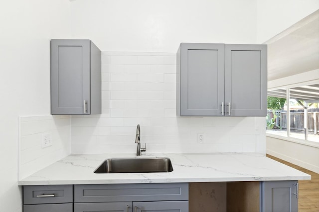 kitchen with gray cabinetry, light stone counters, sink, and hardwood / wood-style floors