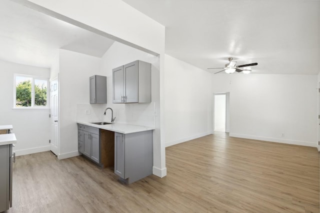 kitchen with ceiling fan, sink, vaulted ceiling, gray cabinets, and light wood-type flooring