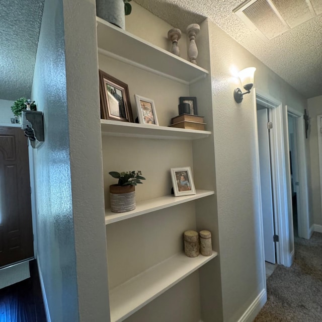 hallway featuring a textured ceiling, carpet flooring, visible vents, and baseboards