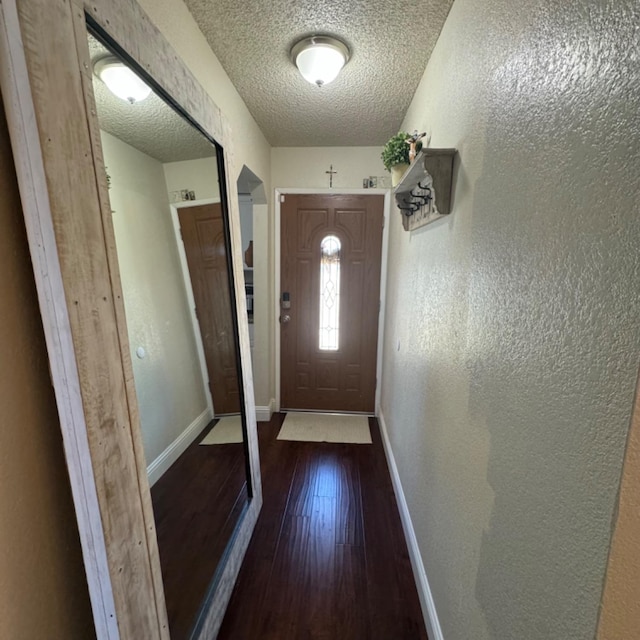 entryway with a textured ceiling, a textured wall, wood finished floors, and baseboards