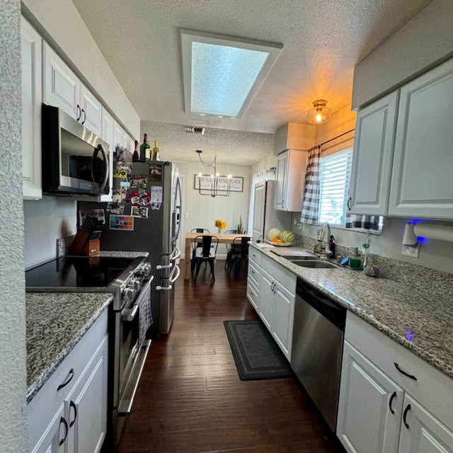 kitchen with dark wood-style flooring, appliances with stainless steel finishes, white cabinets, a sink, and a textured ceiling