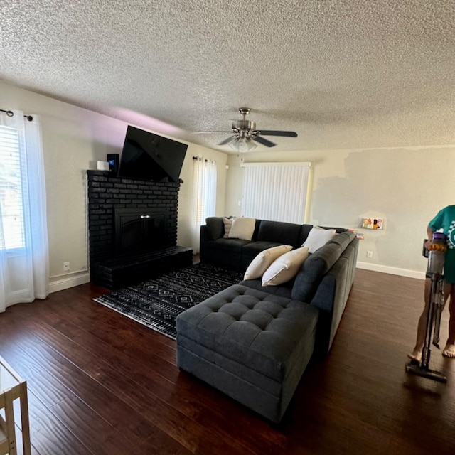 living room with a brick fireplace, a textured ceiling, baseboards, and wood finished floors