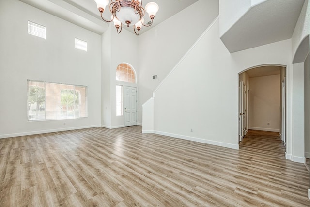 unfurnished living room featuring a notable chandelier, a high ceiling, and light wood-type flooring