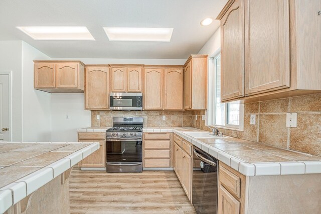 kitchen featuring tile countertops, appliances with stainless steel finishes, light hardwood / wood-style floors, and light brown cabinets