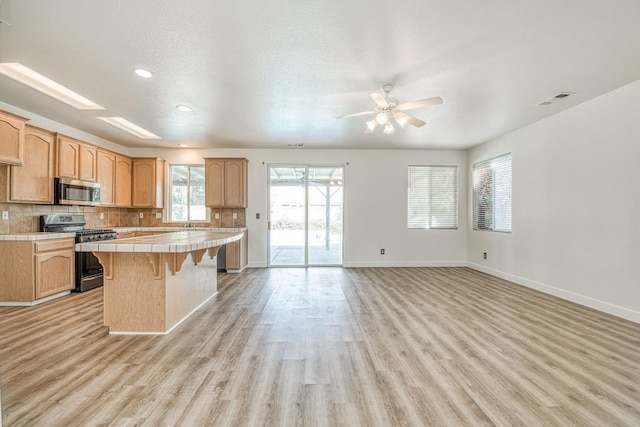 kitchen featuring a breakfast bar, light hardwood / wood-style flooring, stainless steel appliances, tile counters, and a center island