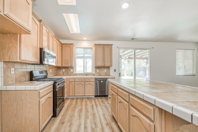 kitchen featuring tile counters, light hardwood / wood-style flooring, stainless steel appliances, backsplash, and light brown cabinetry