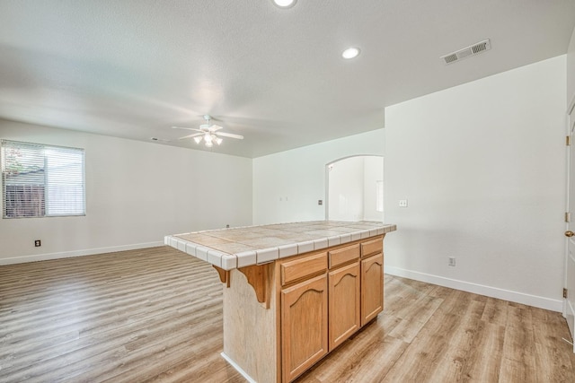 kitchen featuring tile countertops, a center island, a textured ceiling, light hardwood / wood-style floors, and ceiling fan