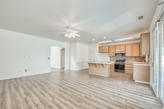 kitchen featuring appliances with stainless steel finishes, a kitchen island, light hardwood / wood-style floors, ceiling fan, and decorative backsplash