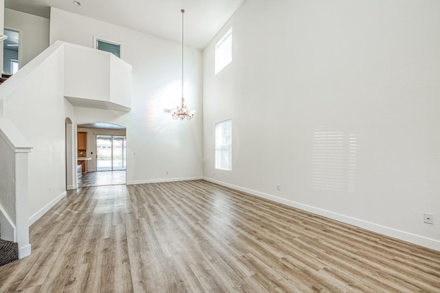 unfurnished living room with a towering ceiling, a chandelier, and light wood-type flooring