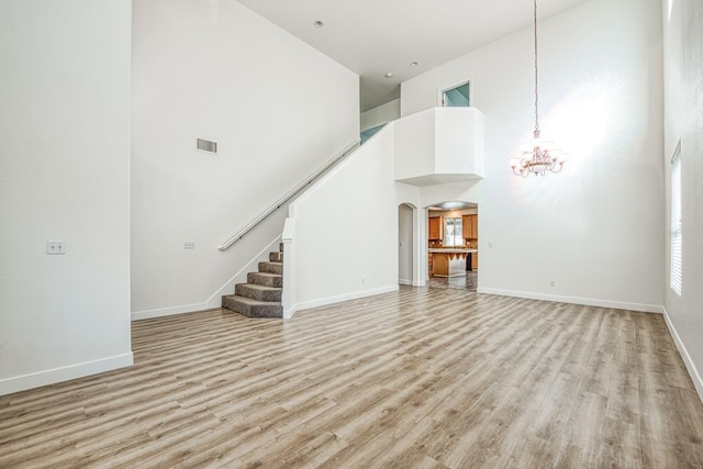 unfurnished living room with an inviting chandelier, light hardwood / wood-style floors, and a towering ceiling