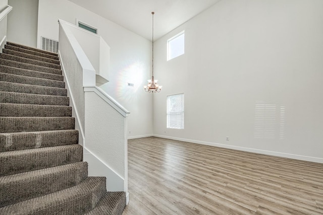 staircase featuring a notable chandelier, hardwood / wood-style flooring, and a high ceiling